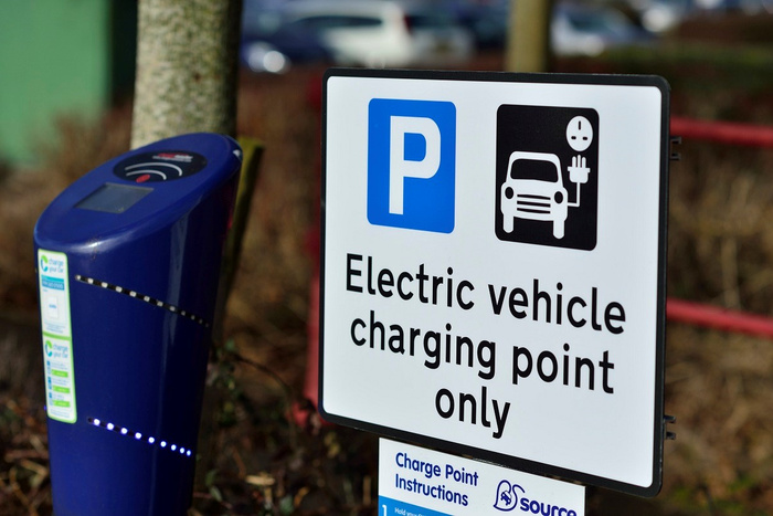 Electric vehicle charging point sign with text 'Electric vehicle charging point only' next to a blue electric car charging station, indicating parking and charging for electric used cars and new cars.