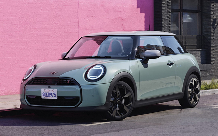 Light green Mini Cooper S hatchback parked on street with black trim and rims, white roof, circular LED headlights, and California license plate 9QKB925, in front of a bright pink wall, representing used cars and new cars options.
