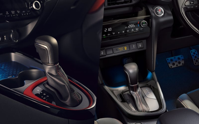Close-up of the gear shift lever in a modern car interior, showcasing a leather-wrapped automatic gear stick with red stitching. The dashboard displays climate control settings with temperature readings of 21.0 and 20.5 degrees Celsius, along with buttons for heated seats and other functions. The interior features a push-start ignition button marked 'GR', sporty pedals, and a sleek black and red trim design, highlighting the advanced and stylish features found in used cars and new cars.