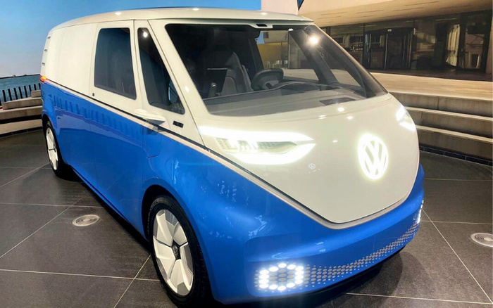 Front and side view of a blue and white Volkswagen electric van with modern LED headlights and illuminated VW logo, displayed indoors on a tiled floor, representing innovative new cars and electric vehicle technology, relevant for buyers interested in used cars and new cars.