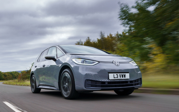 Grey Volkswagen electric car driving on a road surrounded by greenery under a cloudy sky, featuring the license plate L3 VWW, suitable for adverts showcasing new cars and used cars.