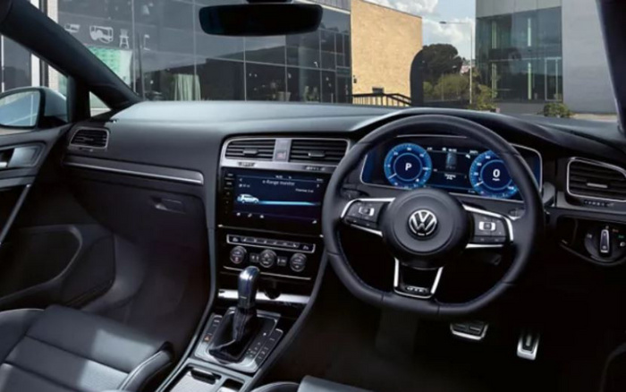 Interior of a modern Volkswagen car showing the dashboard, steering wheel with VW logo, digital instrument cluster displaying 'P' for park and speedometer, central touchscreen with 'e-Range monitor' indicating electric vehicle status, gear shift lever, and black leather seats. The image highlights the sleek and high-tech design appealing to buyers of both used cars and new cars.