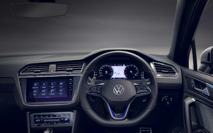 Interior view of a Volkswagen car dashboard showing the steering wheel with Volkswagen logo, digital instrument cluster displaying speedometer and navigation map, touchscreen infotainment system with various menu icons, air vents, and climate control panel. This modern car interior represents features found in both new cars and used cars.