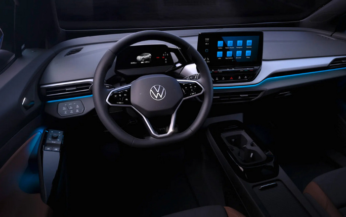 Interior view of a modern Volkswagen car showing the steering wheel with the Volkswagen logo, digital instrument cluster displaying a car graphic, and a touchscreen infotainment system with multiple app icons. The dashboard features sleek design with ambient blue lighting. Suitable for showcasing used cars and new cars.