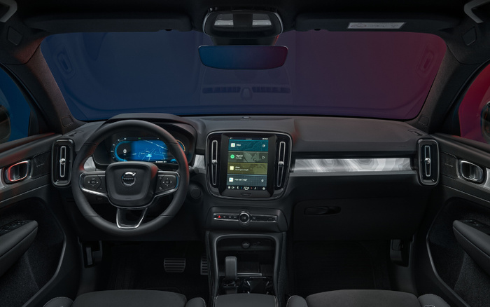 Interior view of a modern car dashboard featuring a digital instrument cluster displaying speed and navigation, a central touchscreen showing music options and navigation apps including Spotify and Maps, and a multifunction steering wheel with the Volvo logo. The photo highlights the advanced technology and design of new cars, suitable for those interested in used cars and new cars with modern infotainment systems.