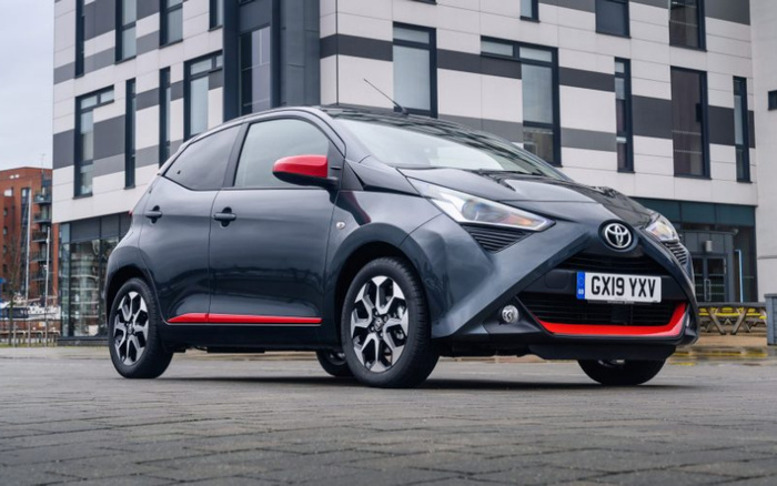 Grey Toyota Aygo with red accents parked on city street in front of modern building, displaying license plate GX19 YXV, showcasing used cars and new cars available for sale.