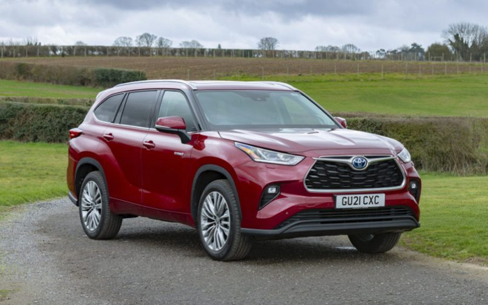 Red Toyota Highlander Hybrid SUV with registration plate GU21 CXC parked on a gravel driveway with green fields and hedges in the background, showcasing a spacious and modern design, ideal for advertising used cars and new cars.
