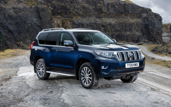 Blue Toyota Land Cruiser Prado SUV with UK license plate TY20 KWX parked on rugged gravel terrain with rocky cliffs in the background, showcasing a new car model suitable for off-road driving, ideal for those searching for used cars or new cars in tough environments.