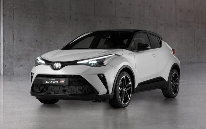White Toyota C-HR GR Sport compact SUV parked indoors against a plain concrete wall, showcasing its sleek modern design and distinctive LED headlights, representing a prime example of new cars available alongside used cars.
