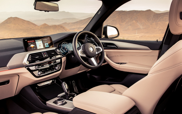 Interior view of a BMW car with beige leather seats, a modern dashboard displaying navigation and media controls, a digital speedometer showing 0 km/h, and a digital screen with options such as 'Navigation', 'Media/Radio', 'Communications', and 'My Vehicle'. The setting includes a desert landscape visible through the windows, highlighting luxury features suitable for buyers interested in used cars and new cars.