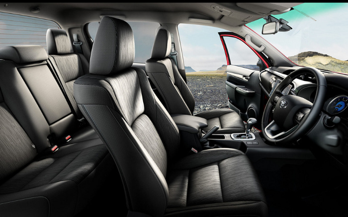Interior view of a modern car with black leather seats, showing the front and rear seats, steering wheel, and dashboard with digital display, parked in an open rocky landscape with a clear sky. The driver side door is open revealing red exterior paint. Ideal for showcasing used cars and new cars with premium interiors.