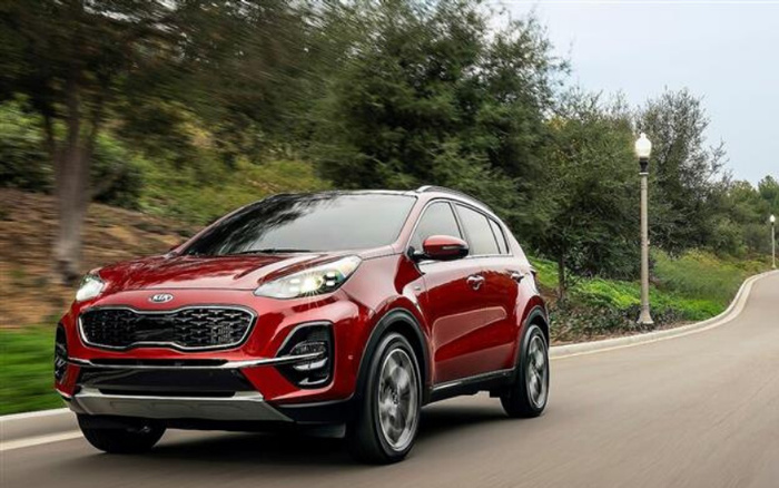Red Kia SUV driving on a tree-lined road with street lamps, showcasing a modern crossover vehicle ideal for new cars and used cars buyers seeking reliable and stylish options.