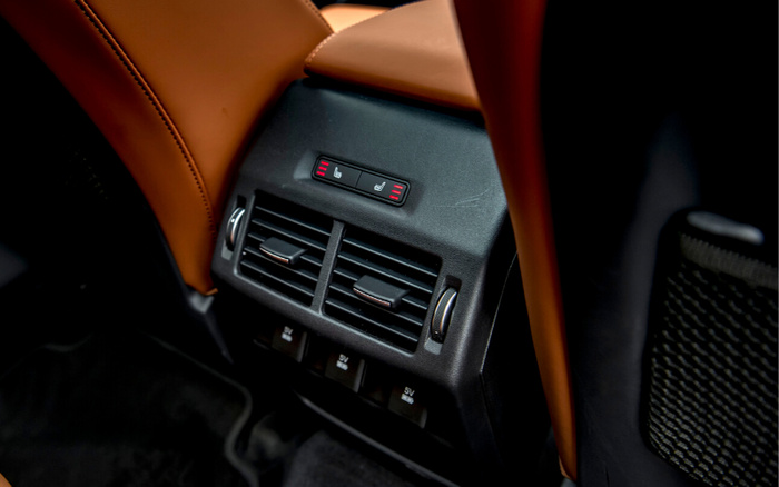 Close-up of rear seat air conditioning vents and heated seat controls with red indicators inside a car featuring brown leather upholstery, showcasing interior details relevant to used cars and new cars.
