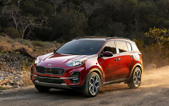 Red Kia Sportage SUV driving on a dirt road in a forested area during daylight with dust trailing behind, showcasing a modern new car model suitable for used cars and new cars buyers.