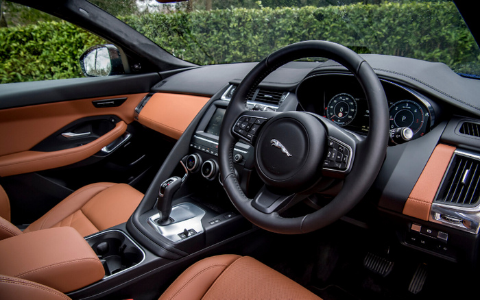 Interior dashboard and steering wheel of a Jaguar car featuring tan leather seats, modern digital instrument cluster, central touchscreen display, and gear shift lever, showcasing the luxury design of used cars and new cars.