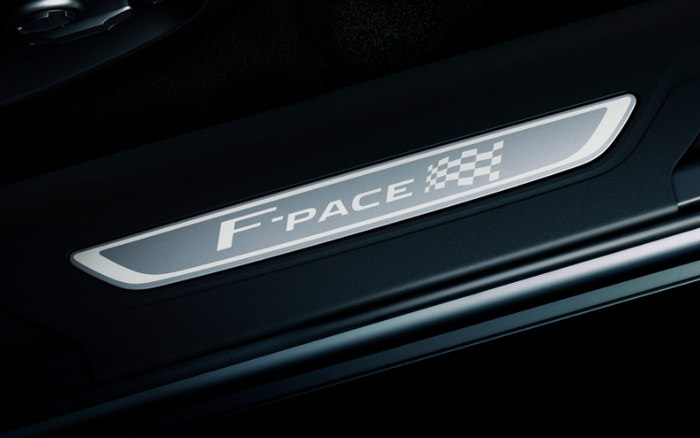 Close-up of the illuminated door sill plate of a Jaguar F-PACE, showing the text 'F-PACE' alongside a racing checkered flag design, highlighting a luxury vehicle interior detail, suitable for used cars and new cars listings.