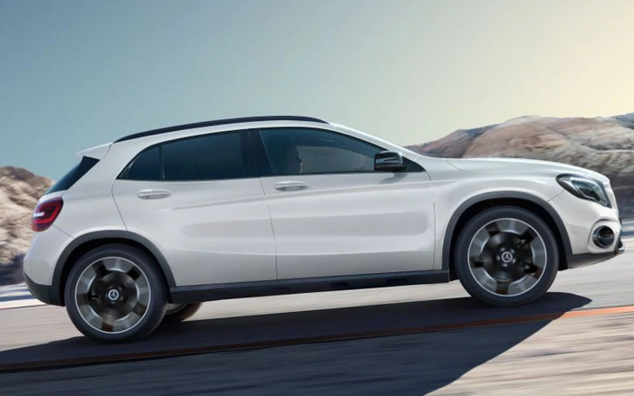 Side view of a sleek white compact SUV driving on a road with mountainous terrain in the background, representing both used cars and new cars options for buyers