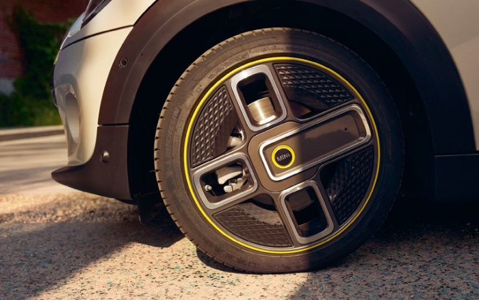 Close-up view of a MINI car wheel featuring a distinctive black and yellow rim design with the MINI logo at the centre, parked on a street. The image highlights a modern, stylish alloy wheel of a new car, suitable for use in advertisements or promotions related to used cars or new cars.