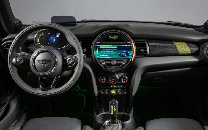 Interior dashboard and steering wheel of a modern Mini car featuring a digital speedometer displaying zero mph, a round central infotainment screen showing a menu with options including Off-peak charging for departure, Self departure time, and Settings charging control, plus controls for air conditioning, media, and gear shift. Suitable for used cars and new cars looking for advanced digital features.