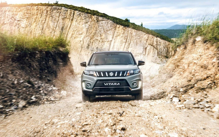 Silver Suzuki Vitara SUV driving on a rugged dirt road with rocky cliffs on both sides under a partly cloudy sky, showcasing a new car model suitable for off-road adventures, ideal for buyers interested in used cars and new cars.
