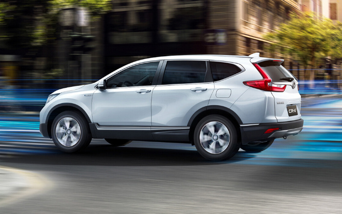 Silver Honda CR-V SUV driving on a city street with blurred buildings and trees in the background, showcasing a modern and sleek design ideal for both used cars and new cars buyers.