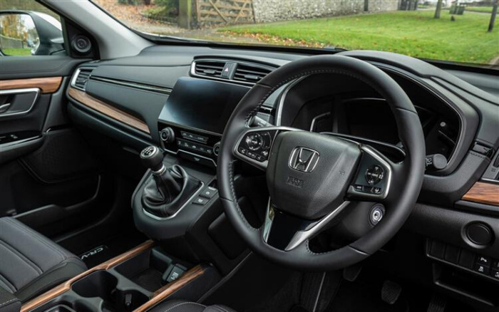 Interior view of a Honda car showing the steering wheel with Honda logo, manual gear stick, modern dashboard with touchscreen display, and black leather seats with wood trim accents, highlighting the features typical of used cars and new cars.