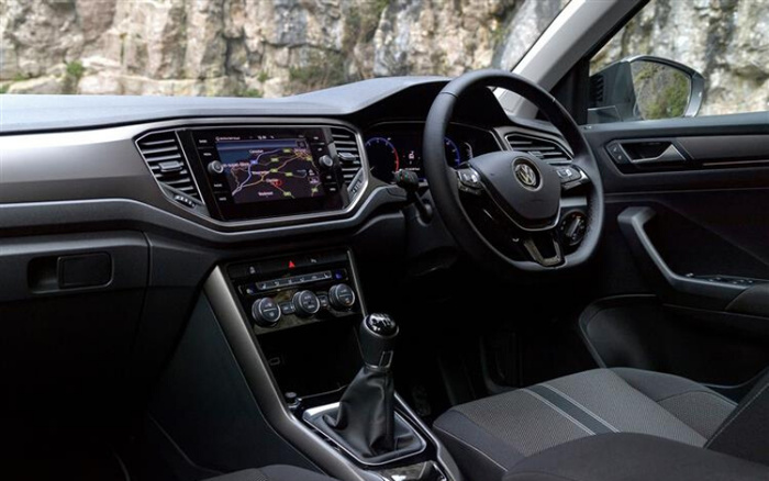 Interior view of a modern car featuring a right-hand drive steering wheel with Volkswagen logo, a touchscreen navigation system displaying a map, manual gear shift, and climate control dials. The photo highlights the dashboard, front passenger seat, and driver controls, suitable for used cars and new cars.