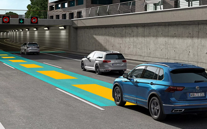 Three Volkswagen cars, including a blue Volkswagen Tiguan at the front, driving on a multi-lane road entering a tunnel with a concrete wall on the right. The blue Tiguan has a visible license plate reading 'WOB TI 310'. Overhead electronic signs display a speed limit of 60 with one green arrow and one red cross above the left lanes. The road features blue and yellow markings on the middle lane. The image represents modern vehicles that could be used or new cars.