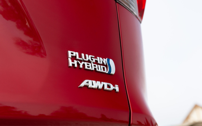 Close-up of rear side of a red car showing chrome badges with the text 'PLUG-IN HYBRID' and 'AWD-i', indicating a plug-in hybrid all-wheel drive vehicle, relevant for buyers interested in used cars or new cars with advanced hybrid technology.