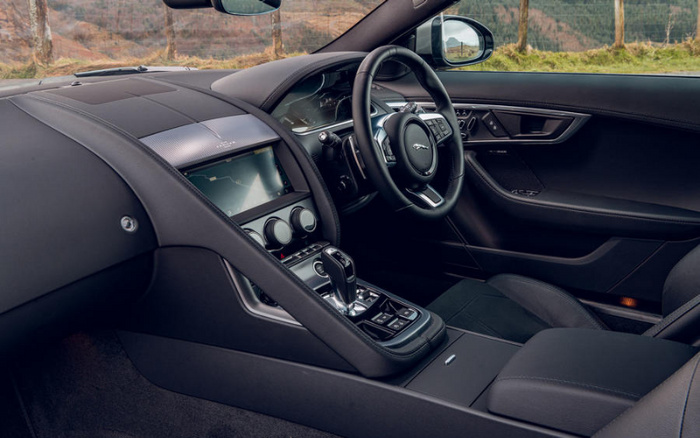 Interior of a Jaguar car showing the steering wheel with the Jaguar logo, digital dashboard, centre console with touchscreen display, climate control knobs, and gear shift lever, highlighting the luxurious design and features relevant for buyers of used cars and new cars.